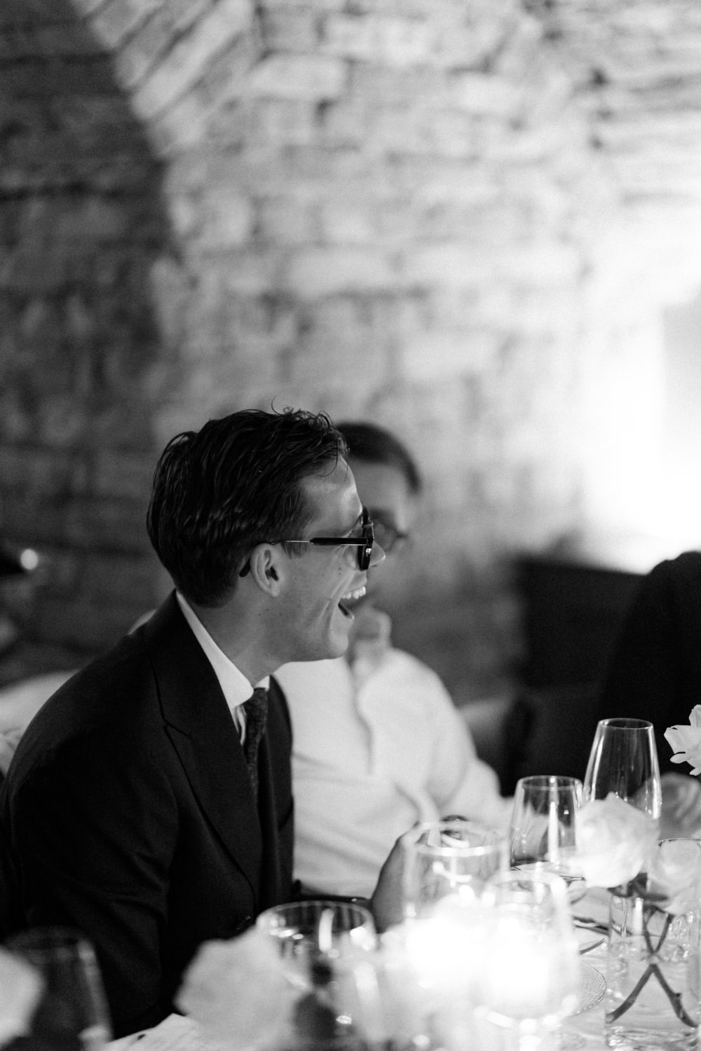 Wedding guest in a suit laughing during dinner at a candlelit reception.