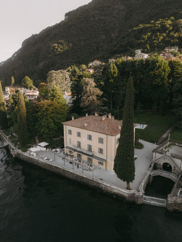Aerial drone view of villa aura del lago destination wedding on Lake Como, framed by cypress trees and forested mountains.